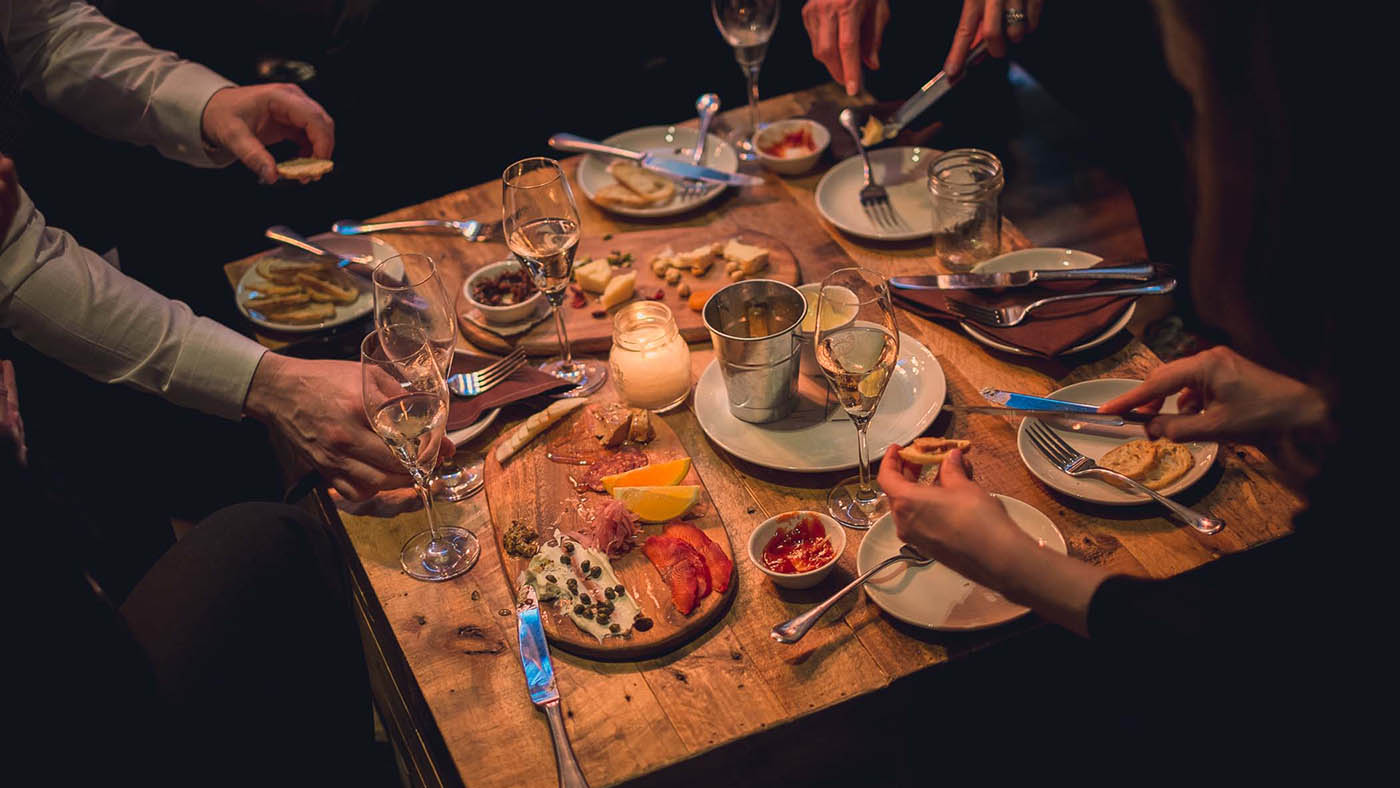 Table top with food, wine glasses, and people's hands eating.